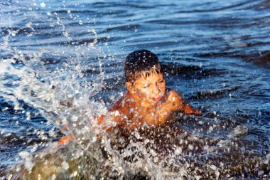 Happy boy splashing in the waves of the Baltic Sea on a bright summer day in Jurmala, Latvia. Summertime and swimming activities for happy children.