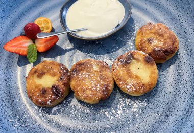 Freshly made cheese cakes with fresh fruit and rustic sour cream with mint on a grey plate. Breakfast. Traditional Slavic dish.