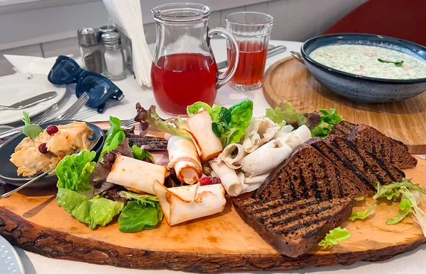 Wooden dish with freshly toasted black bread and various types of lightly salted lard with herbs and summer cold okroshka on fermented baked milk in slavic restaurant, Riga. Latvia