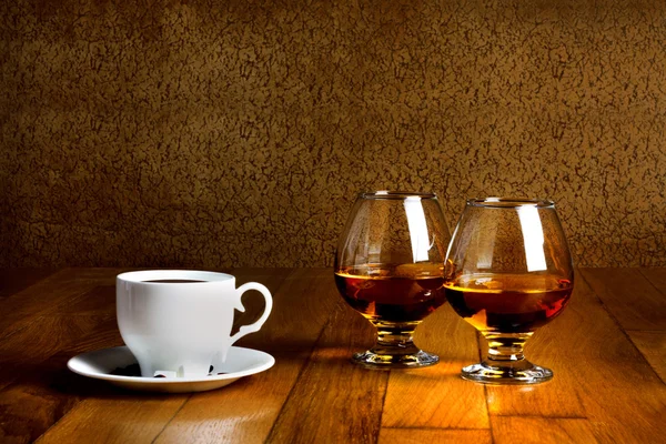 Twee bekers van brandy en kopje warme coffeeon houten oude teller — Stockfoto