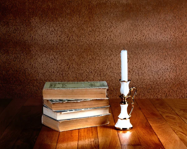 Старая стопка книг с подсвечником и горящей свечой на полу. — стоковое фото