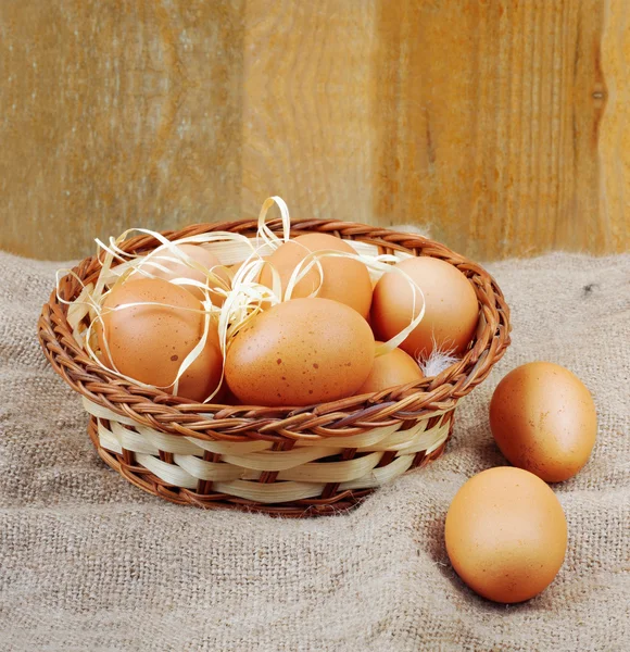 Fresh chicken eggs in straw nest on wooden wall background — Stock Photo, Image