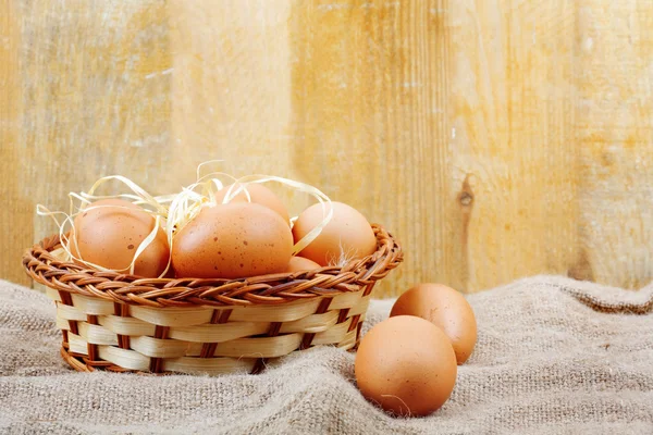 Fresh chicken eggs in straw nest on wooden wall background — Stock Photo, Image