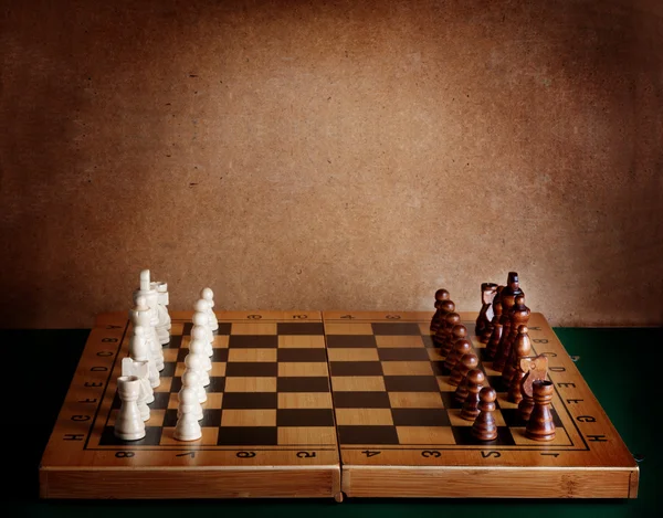 Placa de xadrez de madeira com figuras na mesa verde e parede velha — Fotografia de Stock