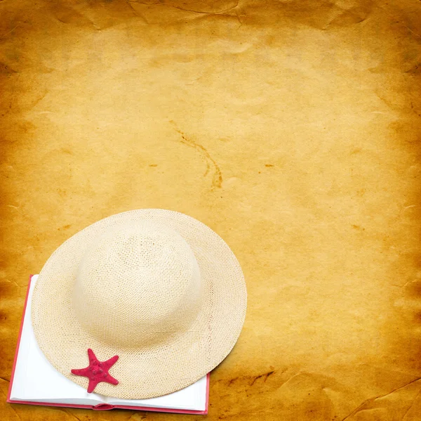 Straw hat with book and red starfish on shabby paper background — Stockfoto