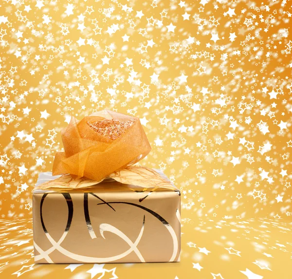 Gift box in gold wrapping paper on a beautiful  abstract backgro — Stock Photo, Image