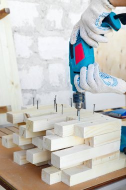 Dolap ustası, matkap, çivi ve çekiçle ahşap mobilyalar yapıyor. Ev yapımı atölyede.