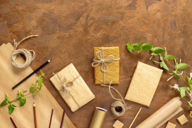 Kağıt ambalajlı hediyeler, klasik sarı paket kağıtları, rulo, ip ve süsleme için kalemler. Altın arka planda çiçekli yeşil hanımeli dalları.