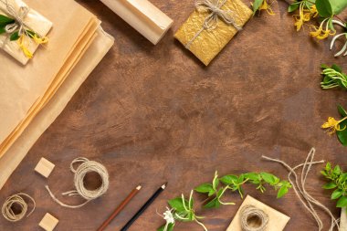 Kağıt ambalajlı hediyeler, klasik sarı paket kağıtları, rulo, ip ve süsleme için kalemler. Altın arka planda çiçekli yeşil hanımeli dalları.