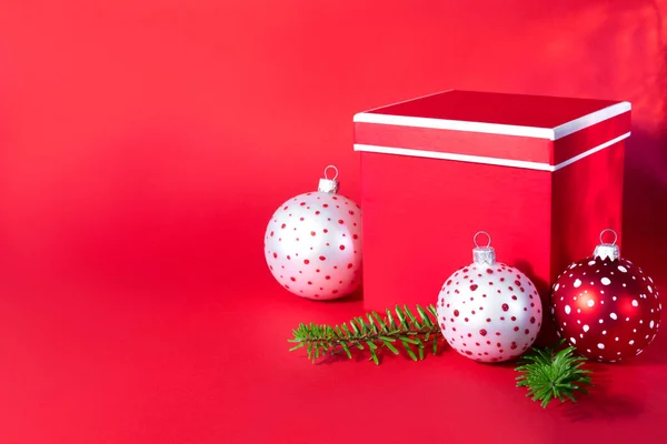 赤い紙の背景に木の枝を持つ多色のクリスマスボールとギフトボックス 新年のクリエイティブグリーティングカード — ストック写真