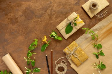 Kağıt ambalajlı hediyeler, klasik sarı paket kağıtları, rulo, ip ve süsleme için kalemler. Altın arka planda çiçekli yeşil hanımeli dalları.