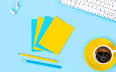 Laptop, aksesuarlar ve mavi arka planda bir fincan kahveli kalem. Çalışma yerinin düzlüğü. 