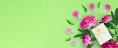 Bouquet of beautiful pink peonies with gift boxes in wrapping paper on green background. Greeting card for the holiday. Creative background with copy space for text.