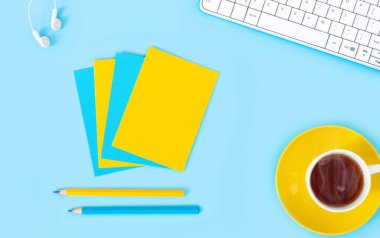 Laptop, aksesuarlar ve mavi arka planda bir fincan çay olan kalem. Çalışma yerinin düzlüğü. 