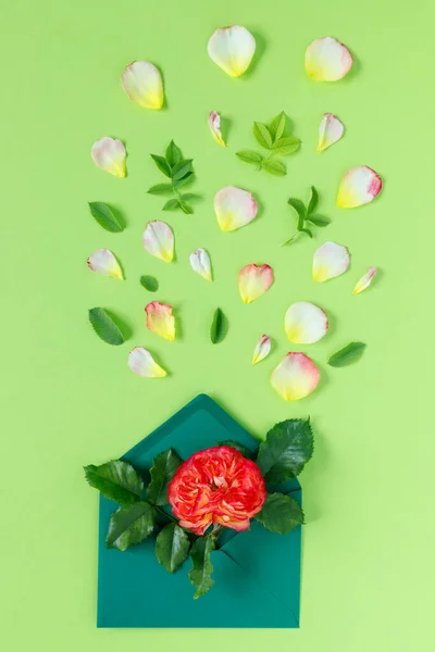 緑の背景に封筒に赤いバラの花束 春休みのミニマルなコンセプト — ストック写真