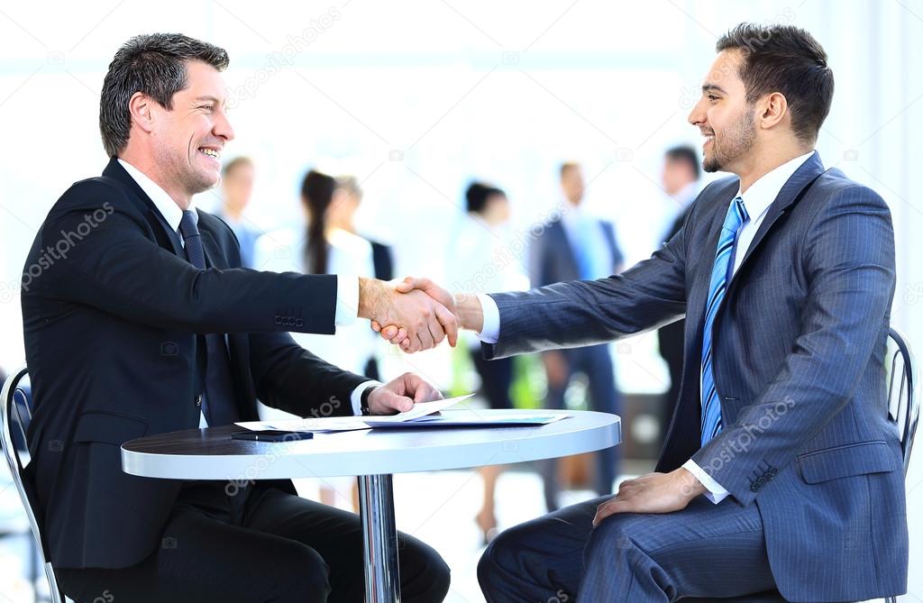 Business colleagues sitting at a table during a meeting with two male executives shaking hands