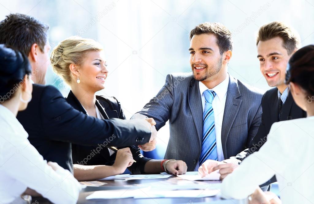 Business colleagues sitting at a table during a meeting with two male executives shaking hands