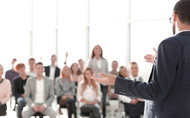 Kapat. Konuşmacı konferans odasında seyircilerin önünde duruyor.