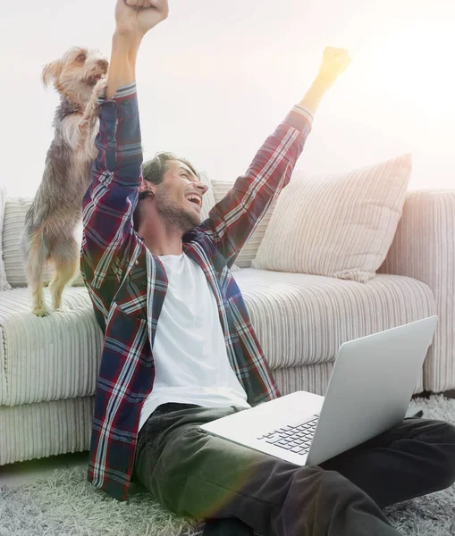 Gelukkig guy jubelt met zijn hond zitten in de buurt van de bank in de woonkamer. — Stockfoto