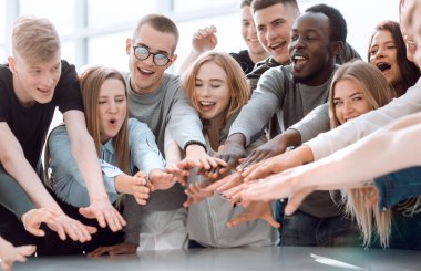 Bir grup gülümseyen genç insan ellerini birleştiriyor.