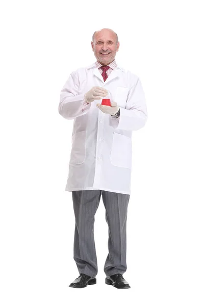 Зрелый ученый с седыми волосами и бородой в белом халате стоит с мензуркой в руке и проводит медицинский тест — стоковое фото
