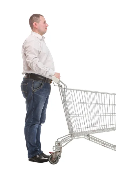 Full length άποψη πλευρά του όμορφος νεαρός άνδρας στέκεται με τρόλεϊ ψώνια και κοιτάζοντας την κάμερα — Φωτογραφία Αρχείου