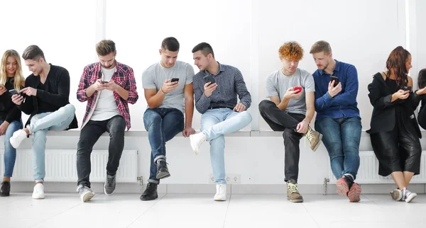 Grupo de jóvenes casuales con teléfonos inteligentes sentados en una fila . — Foto de Stock