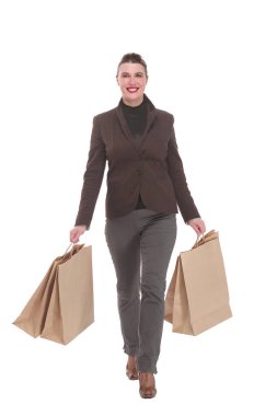 Alışveriş torbaları ve gülümsemeyle yürüyen genç bir kadının tam boy portresi.