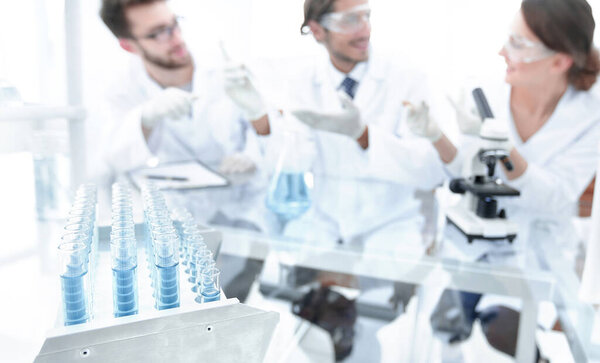 background image is a group of microbiologists studying the liquid in a glass tube.