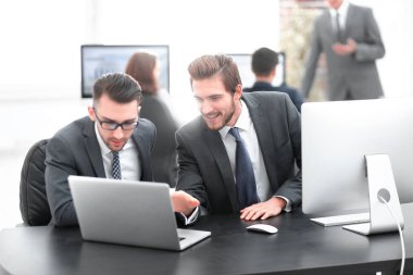 İki odaklanmış iş arkadaşı modern bir ofiste bir masada oturmuş belgeler üzerinde tartışıyorlar.