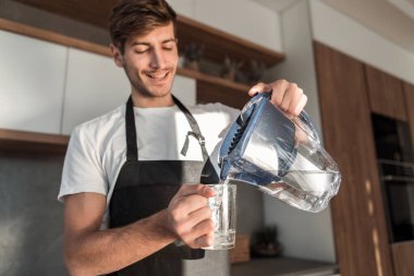 Kapat. Genç bir adam bardağa temiz su döker.