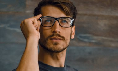 Adam Studio çapraz kollar ile ayakta ve uzağa bakarak gözlük gülümseyen. İzole gri arka plan