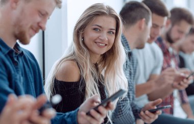 Kapat. Akıllı telefonları olan bir grup genç bir sırada oturuyor.