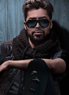 Ahşap duvarda güneş gözlüğü takmış yakışıklı bir adamın portresi. Erkek güzelliği, moda.