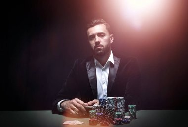Önünde fişleri ve kartlarıyla poker masasında oturan genç adam.