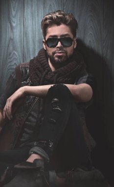 Ahşap duvarda güneş gözlüğü takmış yakışıklı bir adamın portresi. Erkek güzelliği, moda.