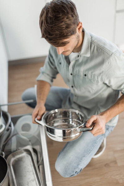 happy young man looking at clean dishes in dishwasher