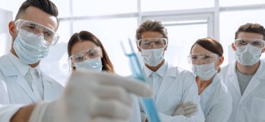 Arkaplan resmi, laboratuardaki sıvılarla fotokopi alanı ile çalışan bir grup tıbbi işçidir.