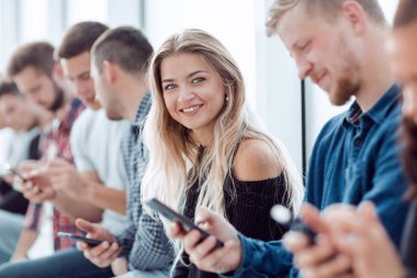 Kapat. Akıllı telefonları olan bir grup genç bir sırada oturuyor.