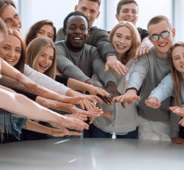 Kapat. Bir grup gülümseyen genç insan ellerini birleştiriyor.