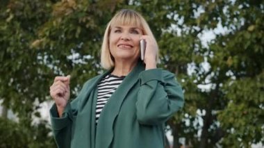 Gülümseyen kadın cep telefonuyla konuşuyor yazın şehir sokağında duruyor.