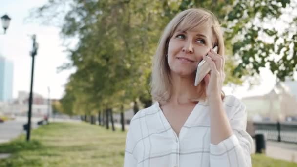 Portret wesołej blondynki rozmawiającej przez telefon komórkowy stojącej na zewnątrz ulicy miasta — Wideo stockowe