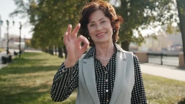 Portrait de femme âgée satisfaite montrant ok geste de la main et souriant à l'extérieur — Video