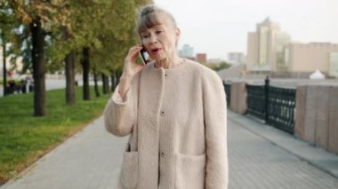 Emekli bir kadının yazın dışarı çıkıp cep telefonuyla konuşması.