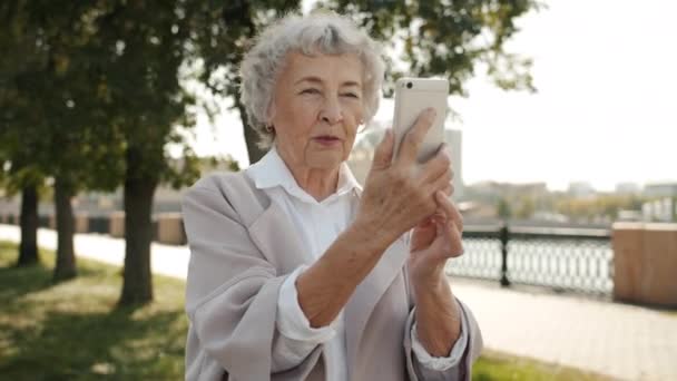 Happy gepensioneerde dame het maken van online video bellen buiten praten en kijken naar smartphone scherm — Stockvideo