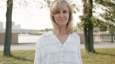 Güzel sarışının yavaş çekimde çekilmiş portresi. Şehrin dışında durmuş gülümsüyor.