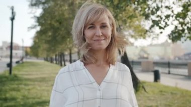 Neşeli sarışın, gülümseyen ve el sallayan rüzgarlı bir günde şehrin dışında duran.