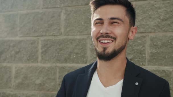 Powolny portret radosnego mieszanego człowieka rasy śmiejącego się na zewnątrz ze ścianą w tle — Wideo stockowe