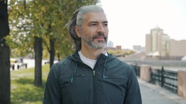 Spor elbiseli neşeli olgun bir adamın yavaş çekim portresi kameraya dönüyor ve dışarıda gülümsüyor.