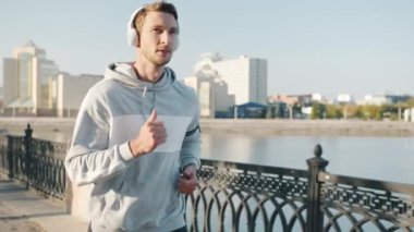 Modern şehirde nehir kenarında koşan çekici genç sporcunun yavaş çekimde portresi.